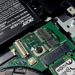 Usługi informatyczne Krystian Widźgowski - Wnętrze laptopa Acer z widoczną płytą główną, baterią i elementami złącz. Detaliczne ujęcie elektroniki podczas naprawy lub modernizacji.