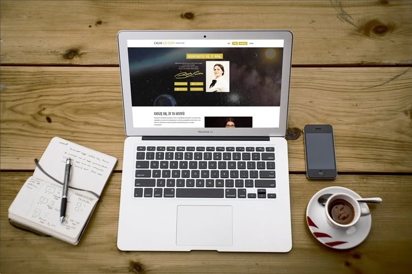 Laptop z otwartą stroną internetową Calm Victory na drewnianym biurku obok notatnika z zapiskami, smartfona i filiżanki kawy espresso.