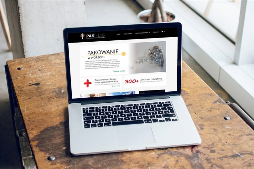 Laptop wyświetlający stronę internetową firmy PAK-LIG z ofertą pakowania w woreczki, umieszczony na drewnianym stole z widoczną rośliną w tle.