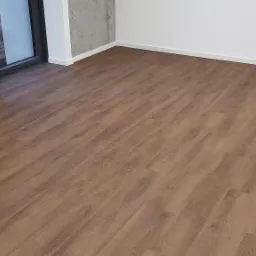 Nowo położona podłoga z paneli imitujących drewno w pustym pokoju z surowymi betonowymi ścianami i świeżo pomalowanymi na biało listwami przypodłogowymi.