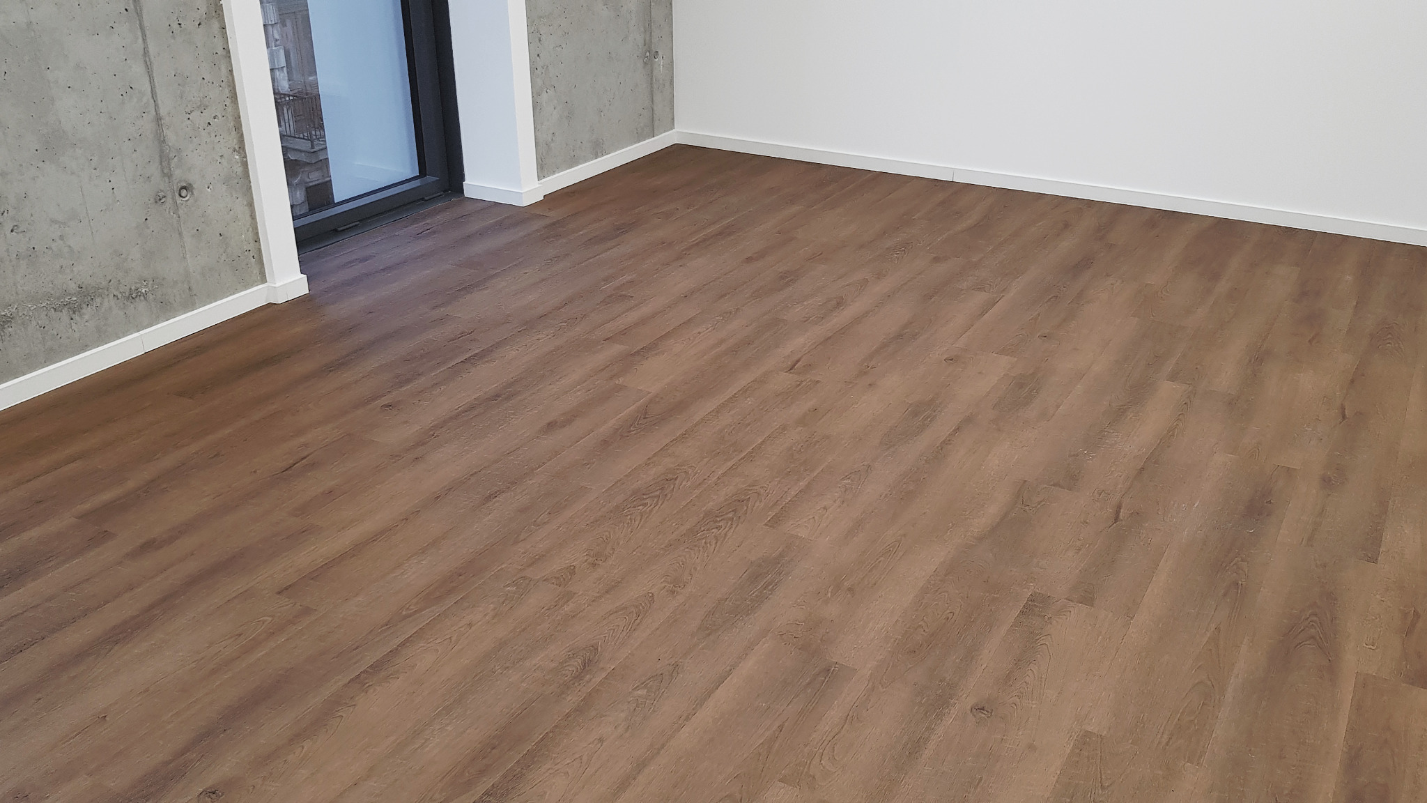 Nowo położona podłoga z paneli imitujących drewno w pustym pokoju z surowymi betonowymi ścianami i świeżo pomalowanymi na biało listwami przypodłogowymi.