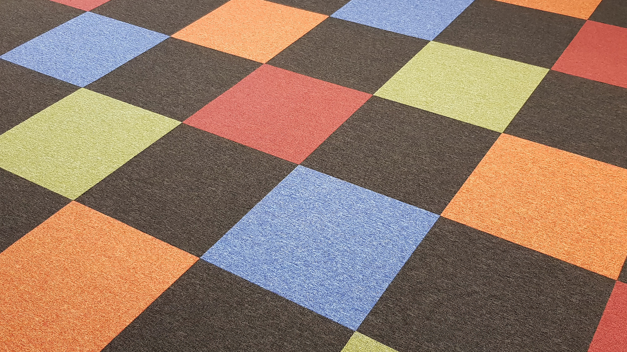 Wzorzysta tapeta w romby: niebieski, zielony, czerwony, pomarańczowy na ciemnobrązowym tle z wyraźną fakturą materiału.