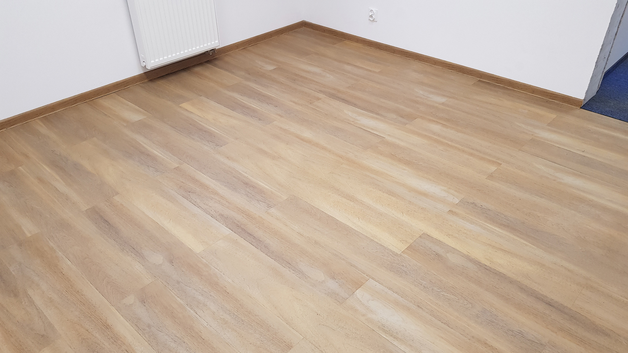 Jasna podłoga panelowa ułożona w pokoju z białymi ścianami i grzejnikiem, widok z góry.