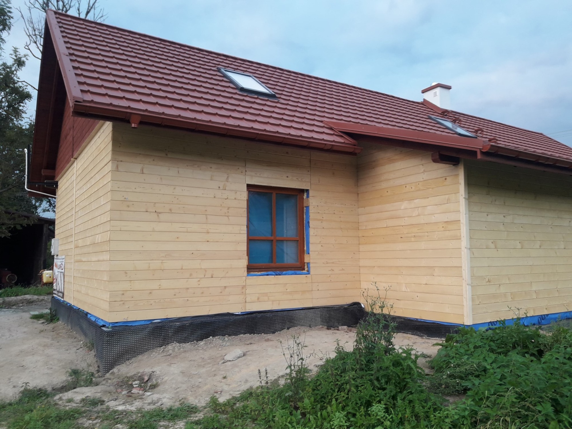 Dom w trakcie budowy z drewnianą elewacją i nowym dachem z czerwonej dachówki z oknami dachowymi.