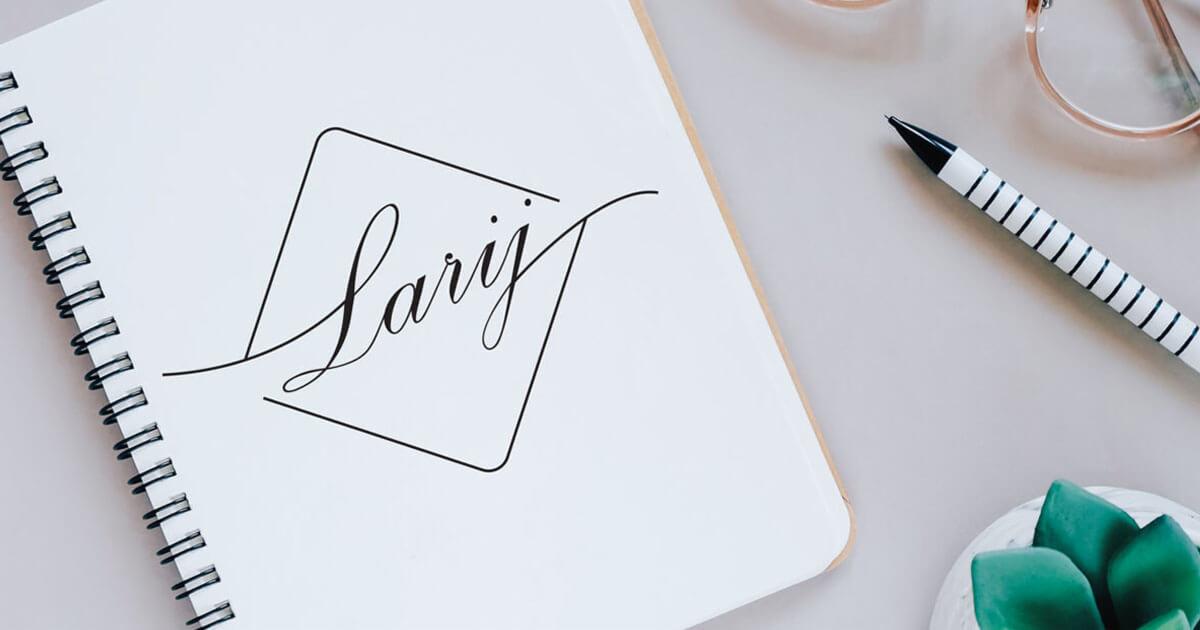 Notatnik z napisem 'Larij' w ozdobnej czcionce, obok długopis w czarno-białe paski, okulary w cienkich, złotych oprawkach i mała roślina w białej doniczce.
