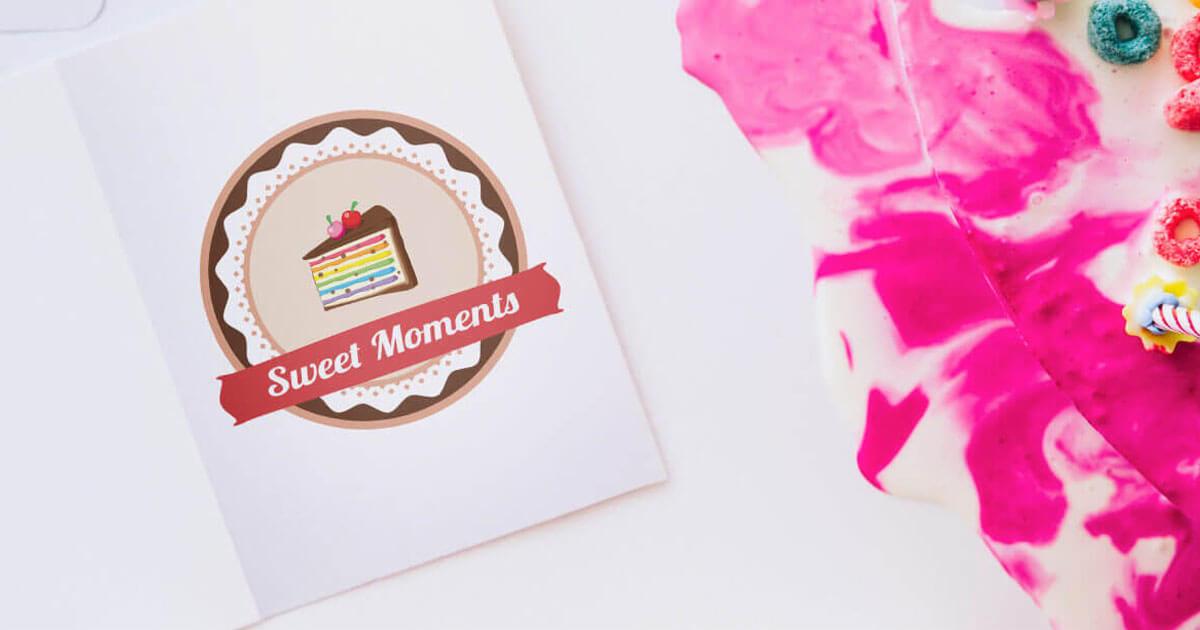 Otwarta kartka z okrągłym logo przedstawiającym kawałek tęczowego tortu z wiśniami, obok różowo-biała masa plastyczna z kolorowymi płatkami śniadaniowymi.