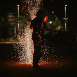 Nocny pokaz fireshow w Siewierzu: artysta żongluje płonącymi rekwizytami, tworząc deszcz iskier na ciemnym tle.