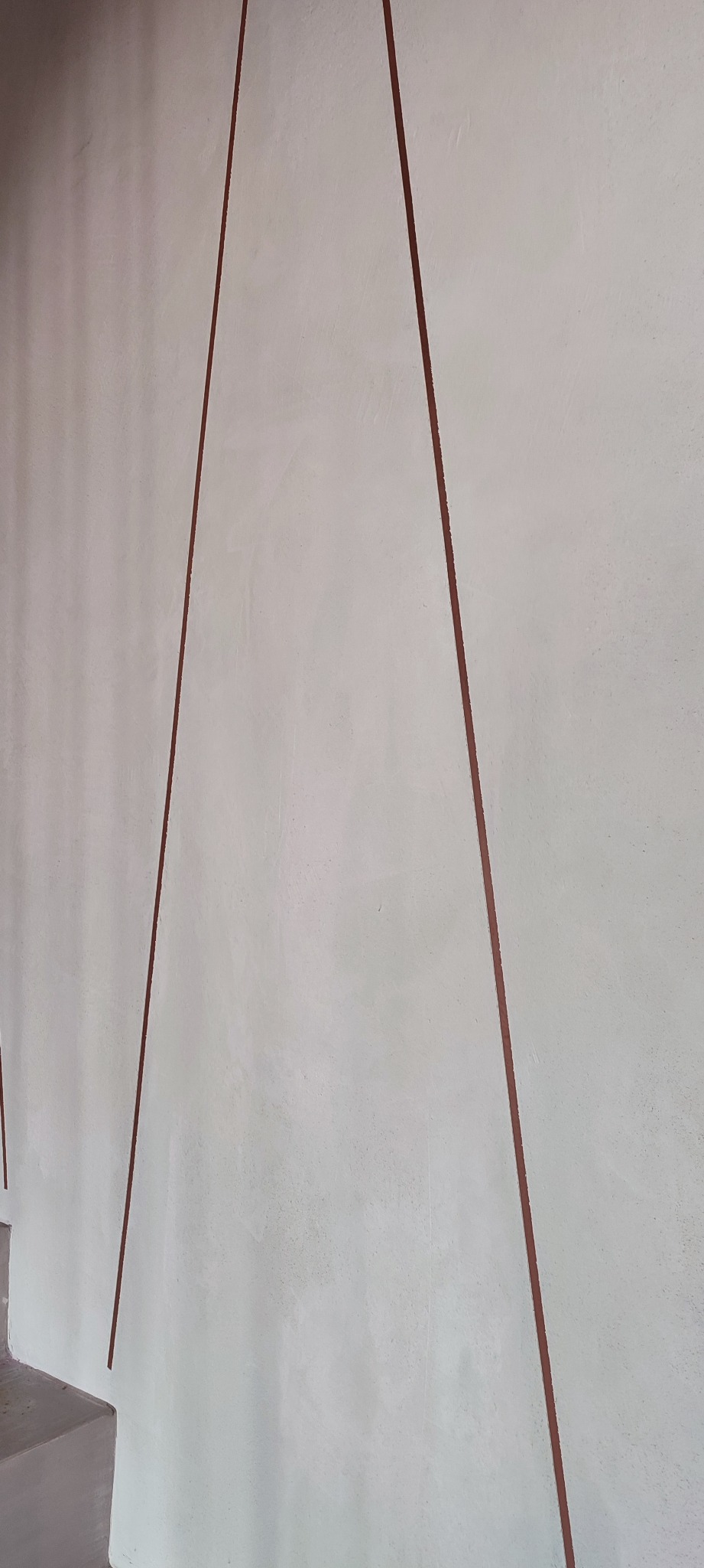 Ściana pomalowana na biało z dekoracyjnymi, pionowymi liniami w kolorze brązowym, widoczne fragmenty schodów.
