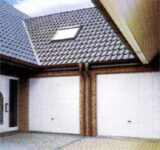 Dwie białe, uchylne bramy garażowe z ceglanymi wstawkami, widoczne od wewnątrz garażu, z widokiem na dach domu z oknem dachowym.