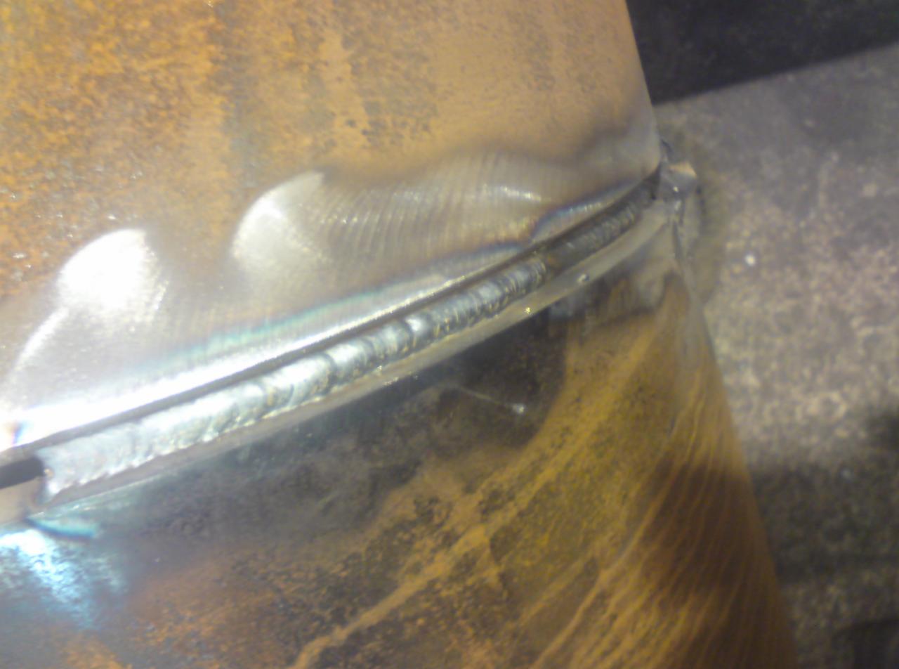 Spoina obwodowa na zardzewiałej rurze stalowej, widoczne ślady obróbki po spawaniu.