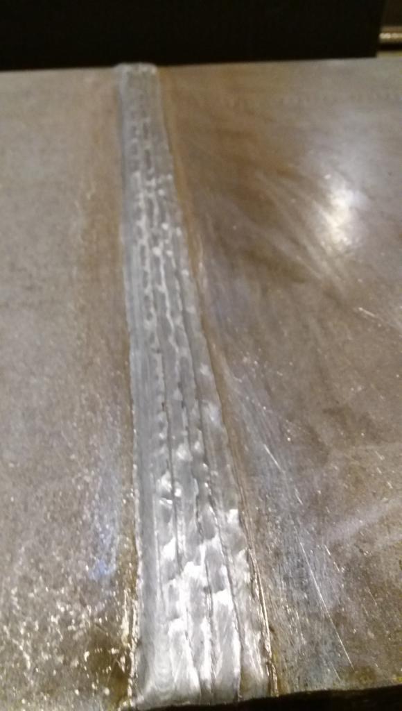 Szlifowany spaw na metalowej płycie, widoczne ślady obróbki i drobne niedoskonałości spoiny.