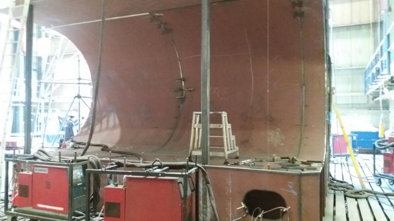 Konstrukcja stalowa w hali produkcyjnej, widoczne spawarki, drabina i fragment rusztowania w tle.