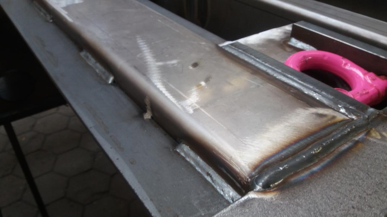 Spoina łącząca metalowe elementy pod kątem, widoczny różowy uchwyt transportowy w tle.