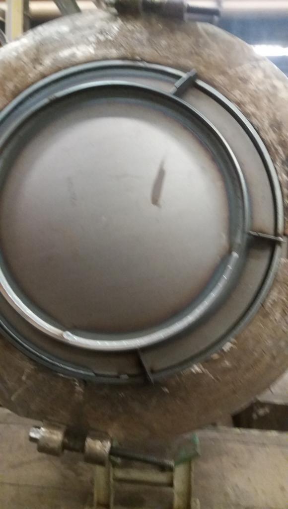 Metalowy zbiornik ciśnieniowy z okrągłym włazem zabezpieczonym pierścieniem i zaciskami, widoczne ślady użytkowania i zabrudzenia.