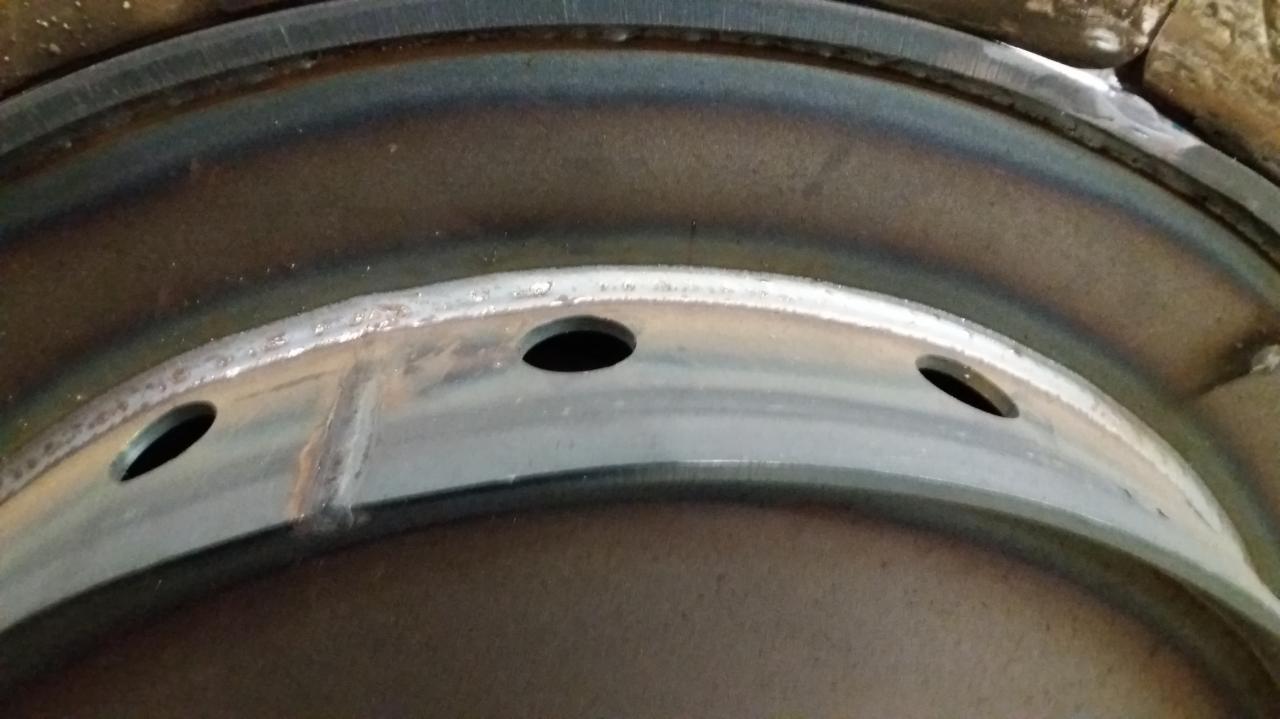 Częściowo spawana metalowa obręcz z trzema otworami, widoczne ślady po spawaniu.