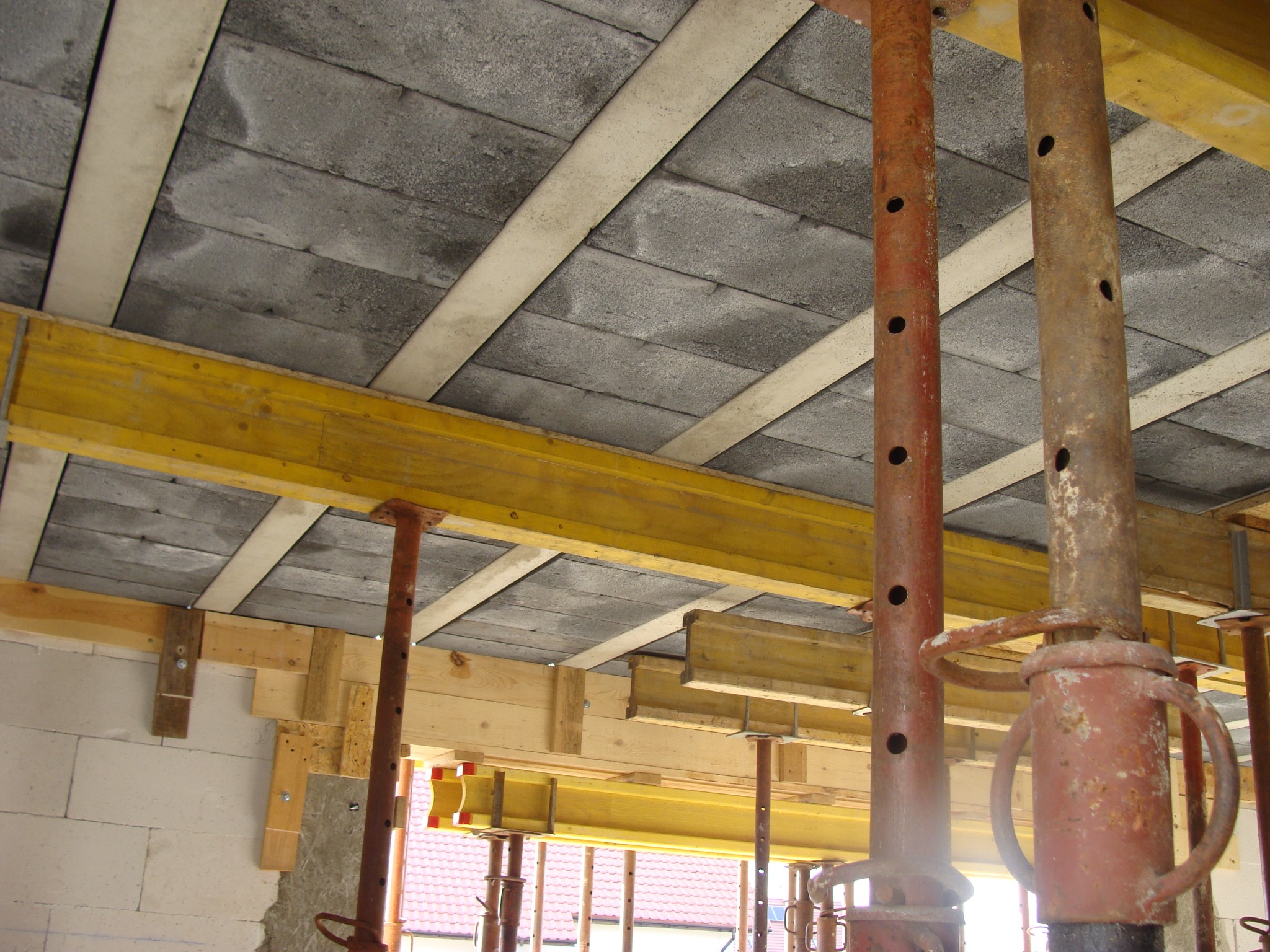 Szare pustaki stropowe Teriva podparte metalowymi stemplami i drewnianymi belkami. Widok z dołu na strop w trakcie budowy domu.