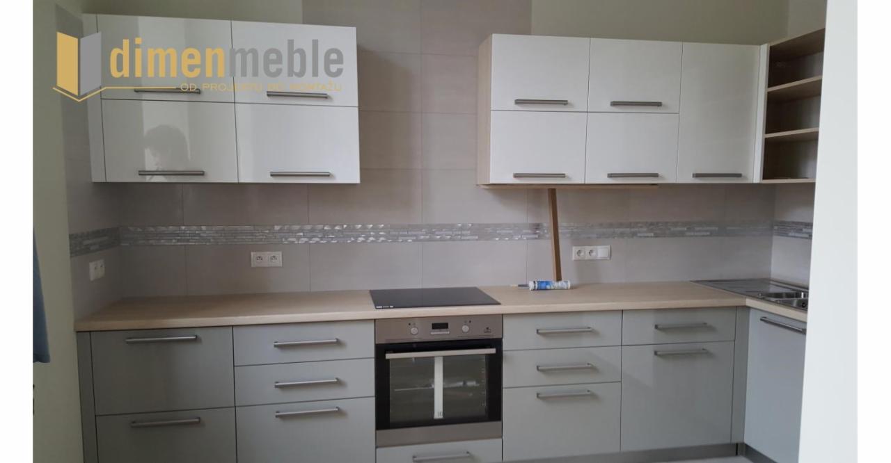 Szare i białe szafki kuchenne z drewnianym blatem, widoczny piekarnik i płyta indukcyjna, na górnych szafkach logo firmy.