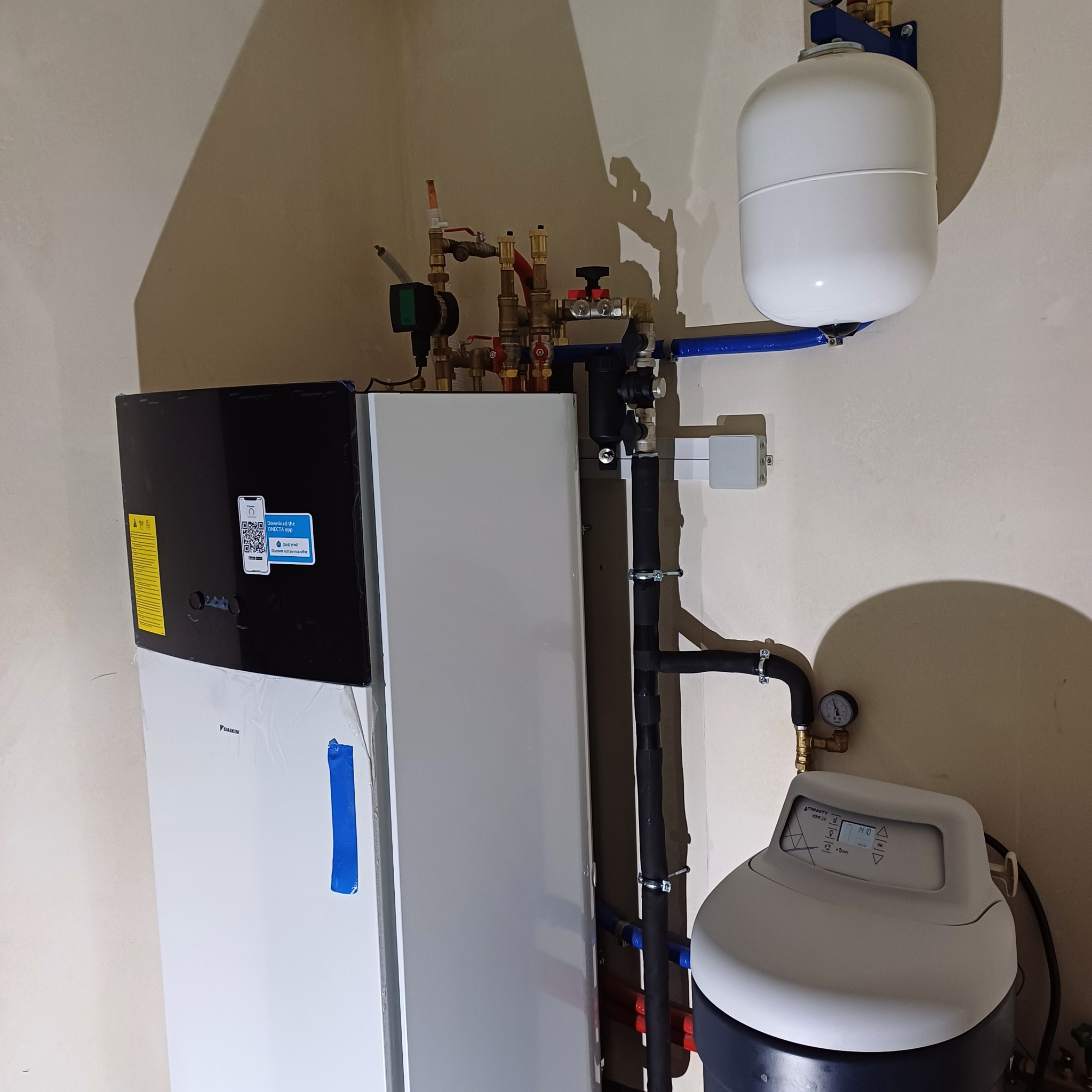 Zestaw urządzeń grzewczych Daikin z podłączonymi rurami miedzianymi i plastikowymi. Widoczny zbiornik wyrównawczy i filtr wody. Część urządzeń jest jeszcze w folii.