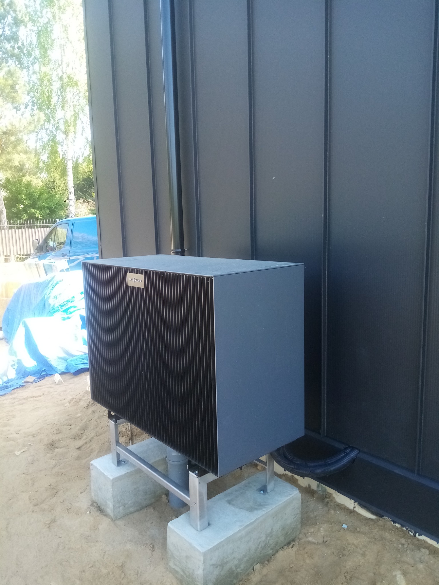 Zamontowany piec gazowy Viessmann na zewnątrz budynku w Płońsku. Piec stoi na betonowych podstawach, widoczna czarna rura odprowadzająca spaliny i czarna ściana budynku.