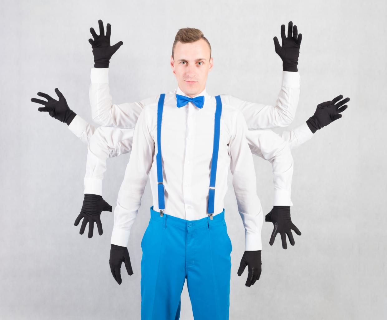 Mężczyzna w białej koszuli, niebieskich spodniach i szelkach, z czterema parami rąk w czarnych rękawiczkach, na szarym tle.
