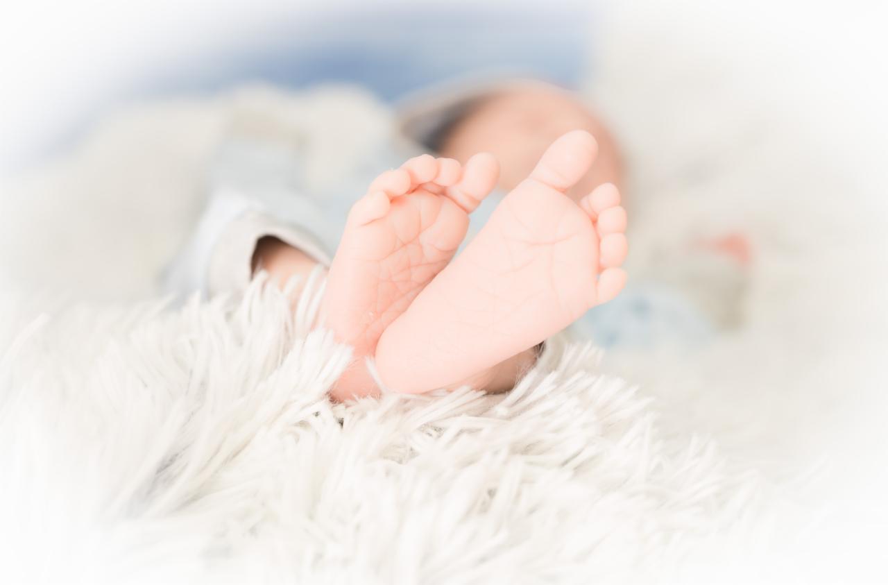 Drobne stópki noworodka na puszystym, białym kocyku, delikatne światło, pastelowe kolory.