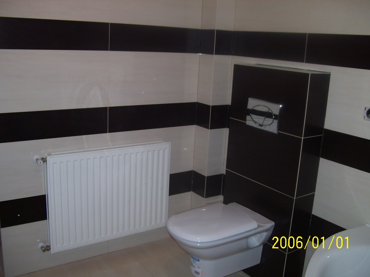 Łazienka z poziomymi pasami z białych i czarnych płytek ceramicznych, wisząca toaleta z zabudowaną spłuczką, biały grzejnik.