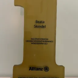 Złota statuetka w kształcie cyfry 1 z napisem Beata Skindel, Najlepszy Dyrektor Obszaru Sprzedaży w Rankingu Menedżerskim 2022, logo Allianz i Kongres Allianz 2023 - Najlepsi z Najlepszych.