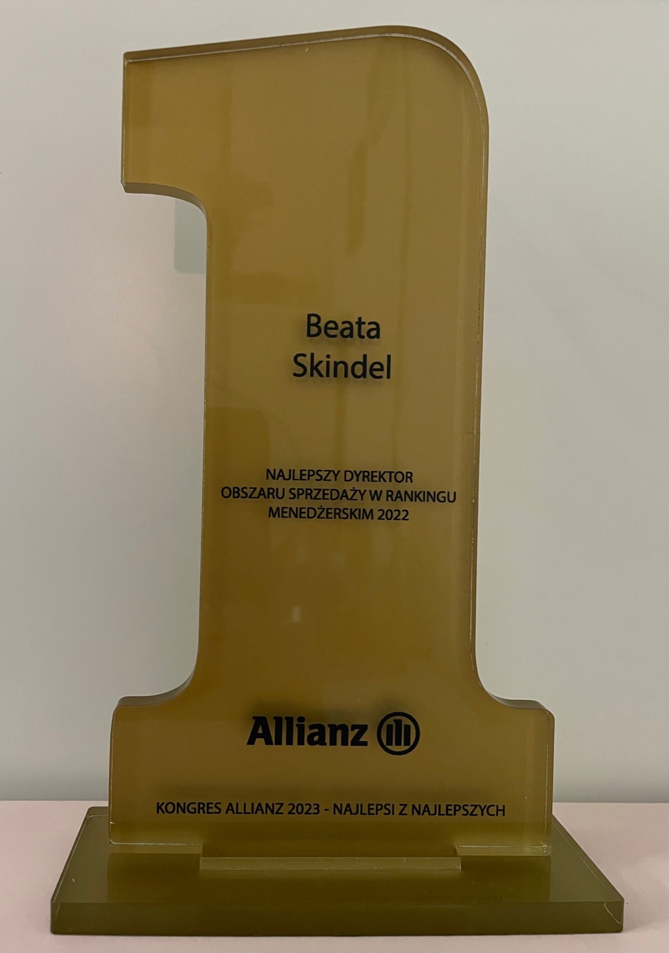 Złota statuetka w kształcie cyfry 1 z napisem Beata Skindel, Najlepszy Dyrektor Obszaru Sprzedaży w Rankingu Menedżerskim 2022, logo Allianz i Kongres Allianz 2023 - Najlepsi z Najlepszych.
