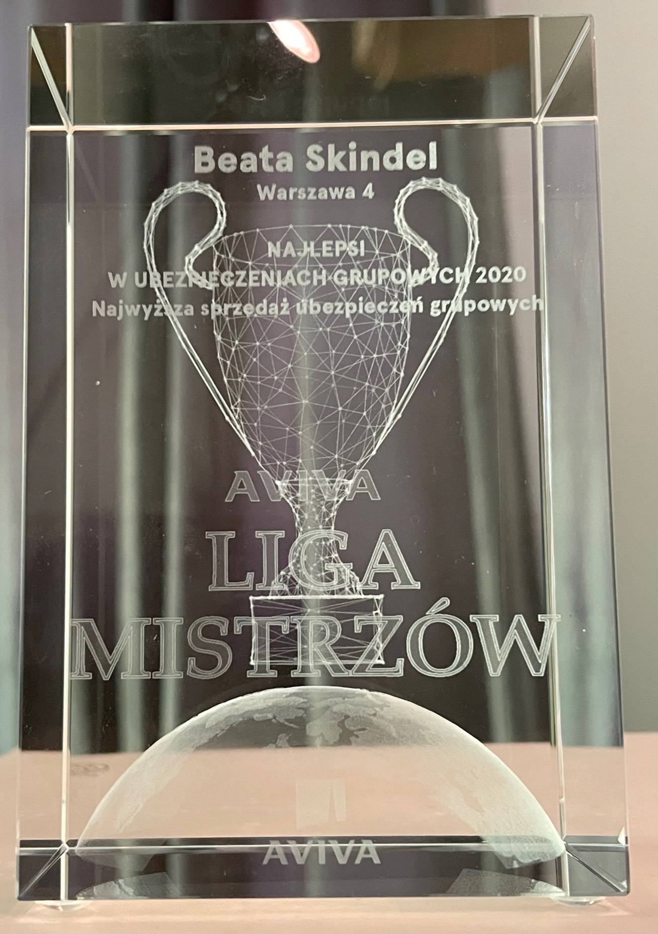 Kryształowa statuetka z wygrawerowanym pucharem i napisem 'Beata Skindel Warszawa 4 NAJLEPSI W UBEZPIECZENIACH GRUPOWYCH 2020 Najwyższa sprzedaż ubezpieczeń grupowych AVIVA LIGA MISTRZÓW AVIVA'...