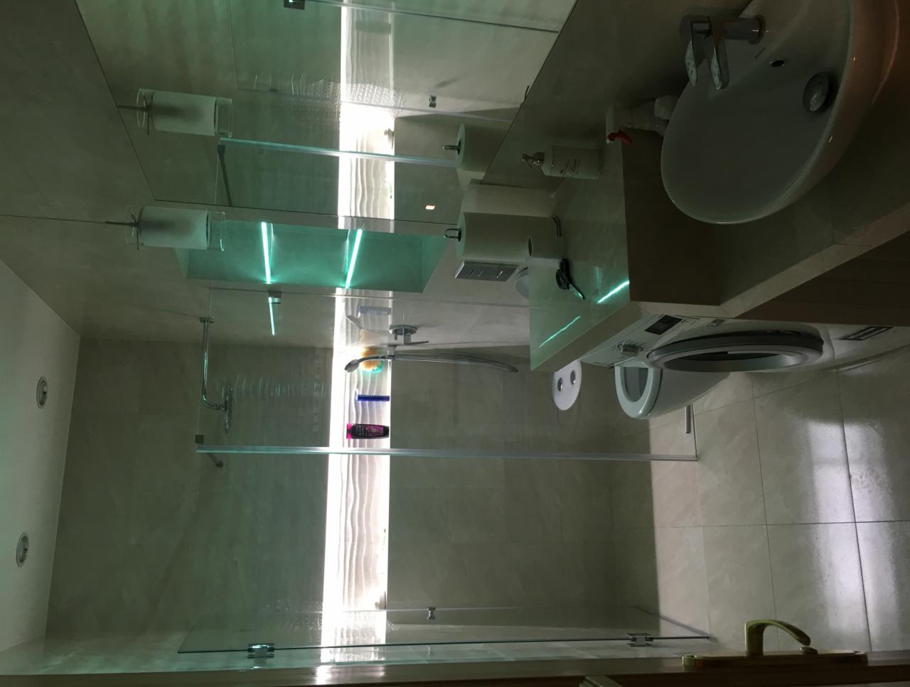 Jasna łazienka po remoncie z kabiną prysznicową ze szklanymi drzwiami, umywalką nablatową i pralką pod blatem, wykończona beżowymi płytkami.