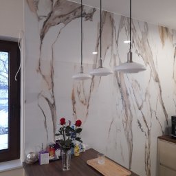 BAJBUD - Ściana w kuchni wykończona płytami imitującymi marmur z trzema wiszącymi lampami nad blatem