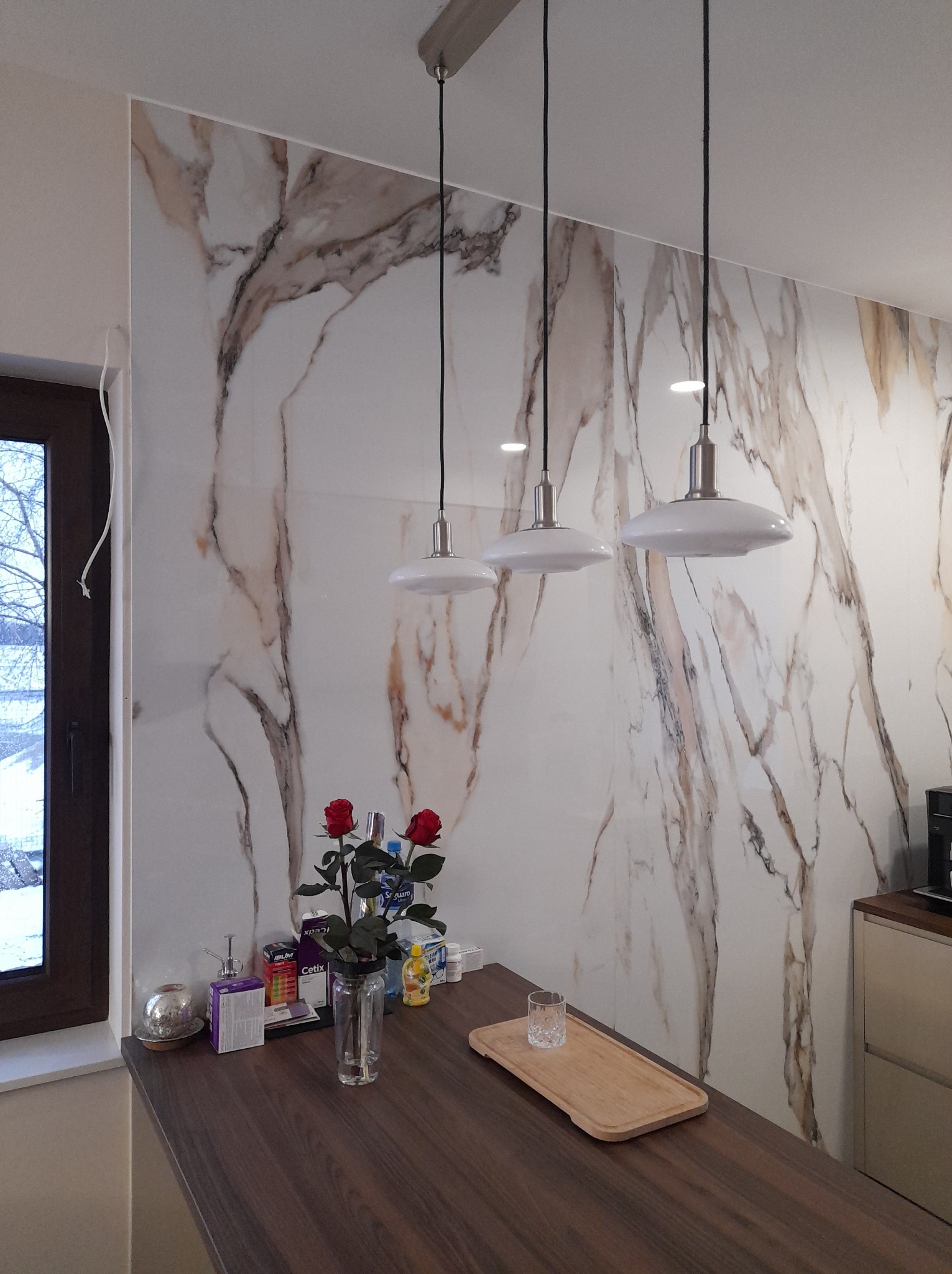 Ściana w kuchni wykończona płytami imitującymi marmur z trzema wiszącymi lampami nad blatem
