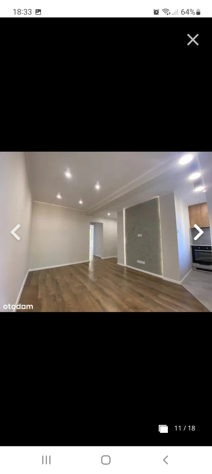 Jasne wnętrze po remoncie: parkiet, ściany w odcieniach beżu, dekoracyjna szara ściana z oświetleniem LED, widoczna zabudowa kuchenna w tle.