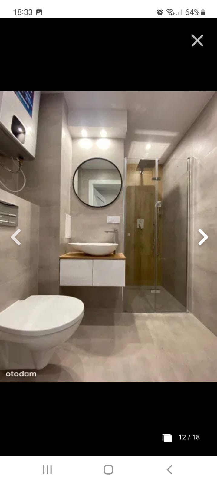 Nowoczesna łazienka w Radomiu z kabiną prysznicową, umywalką nablatową na drewnianej szafce i okrągłym lustrem, wykończona szarymi płytkami.