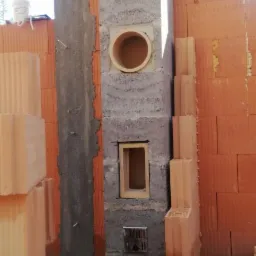 Wznoszony komin z pustaków szamotowych z otworem rewizyjnym i wyczystką, widoczne bloczki ceramiczne na budowie.