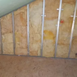 Poddasze w trakcie ocieplania: wełna mineralna między metalowymi profilami, widoczne instalacje elektryczne i fragment podłogi z płyty OSB.