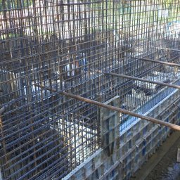 ALTER PROJEKT Sp. z o.o. - Gęste zbrojenie stalowe przygotowane do zalania betonem, widoczny szalunek i wykop pod fundament lub ścianę konstrukcyjną.