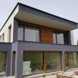 Nowoczesny dom w Mikołowie z szarą elewacją i drewnianymi akcentami, widoczne materiały izolacyjne przy oknie.