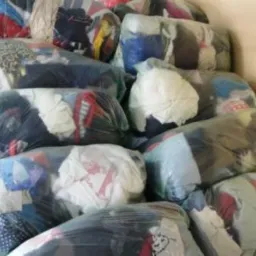 Stos zapakowanych w przezroczyste worki pakietów odzieży używanej, outletowej i posklepowej, ustawionych pod ścianą w magazynie.