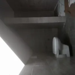 Szara łazienka z podwieszaną toaletą, widok z dołu, płytki na podłodze i ścianach, wnęka pod sufitem wykończona płytkami.