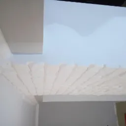 Montaż dekoracyjnej płyty gipsowej na suficie, widoczne niedoskonałości w połączeniach i wykończeniu, sufit częściowo pomalowany na jasny odcień błękitu.