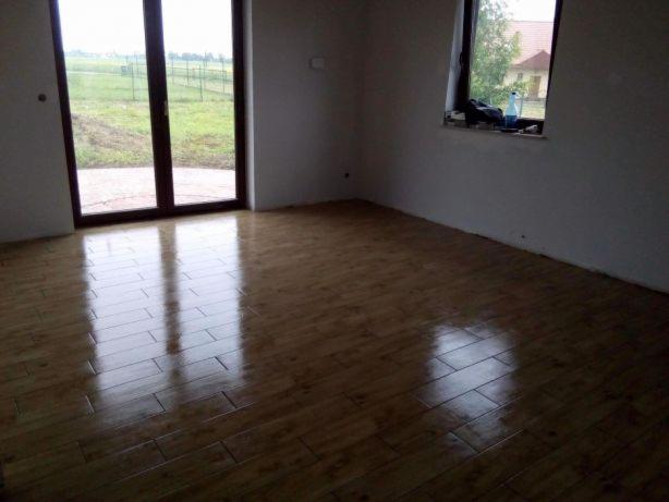 Nowo ułożone, błyszczące panele podłogowe w pustym pokoju z dużym oknem balkonowym i oknem z widokiem na zewnątrz, na parapecie butelka z płynem.