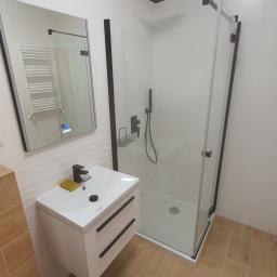 Specmar - Nowoczesna łazienka po remoncie: biała umywalka z czarną armaturą, kabina prysznicowa z czarnymi profilami, lustro z podświetleniem LED i grzejnik drabinkowy.