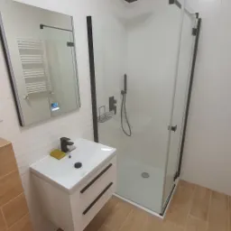 Nowoczesna łazienka po remoncie: biała umywalka z czarną armaturą, kabina prysznicowa z czarnymi profilami, lustro z podświetleniem LED i grzejnik drabinkowy.