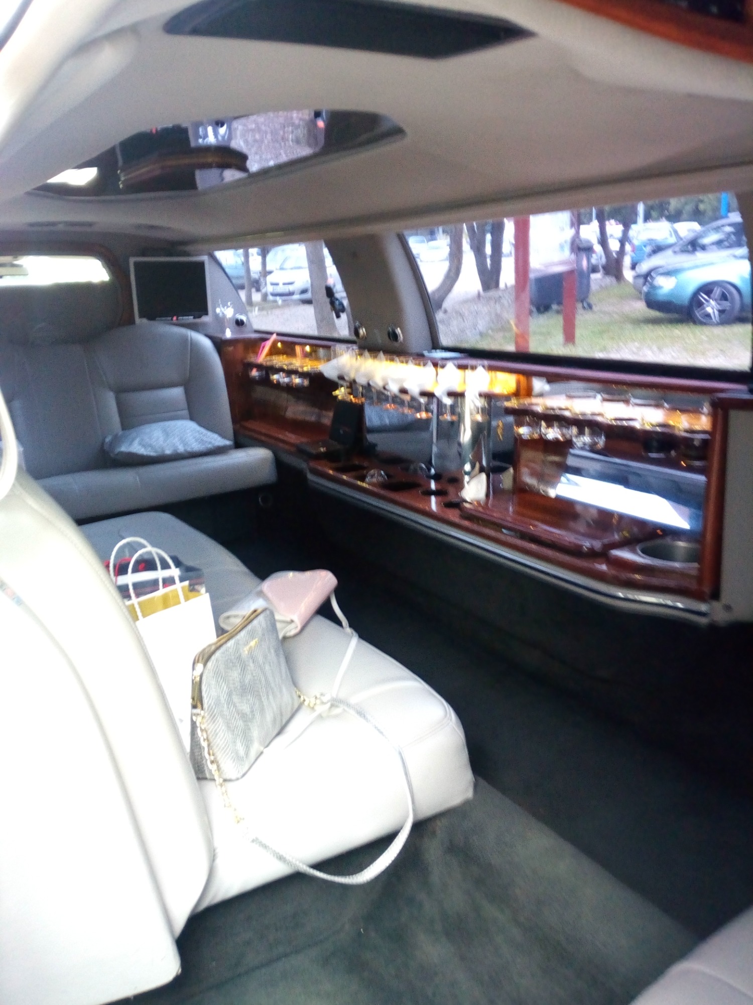 Wnętrze luksusowej limuzyny z barkiem, szklankami, skórzanymi siedzeniami, poduszką i torebkami leżącymi na siedzeniu, widok z perspektywy pasażera.