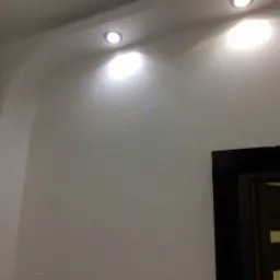 Ściana z gładzią i wbudowanymi punktami świetlnymi w pomieszczeniu w Sierakowicach, widoczna czarna rama drzwi.