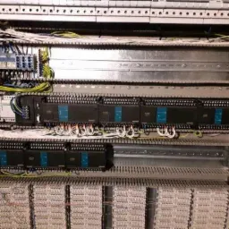 Rozdzielnica elektryczna z modułami sterującymi Siemens, widoczne liczne przewody i złączki, ułożone w uporządkowany sposób w metalowej szafie. Widoczne oznaczenia na modułach.