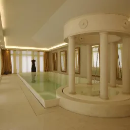 Wnętrze basenu z kolumnami i marmurową posadzką, widoczne lustra w złotych ramach i rzeźba w tle.