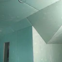 Montaż zielonych płyt gipsowo-kartonowych na poddaszu, widoczne łączenia i mocowania, przygotowanie do dalszych prac wykończeniowych.