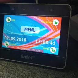 Ekran dotykowy centrali alarmowej Satel z widocznym menu i statusem zabezpieczeń poszczególnych stref: Dom, Stodoła, Pracownia, Domek. Na ekranie widoczna data 07.09.2018 i godzina 17:08:41.